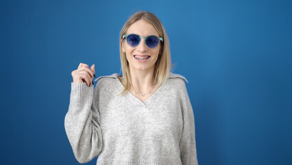 Young blonde woman smiling confident showing braces over isolated blue background