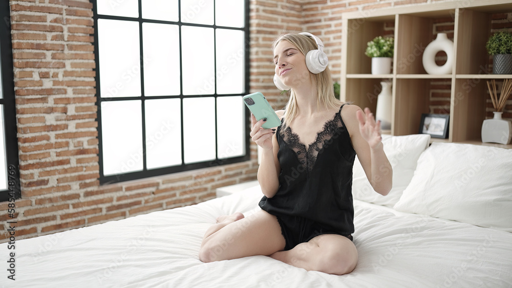 Poster young blonde woman dancing sitting on bed looking sexy at bedroom