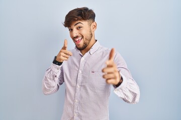 Arab man with beard standing over blue background pointing fingers to camera with happy and funny...