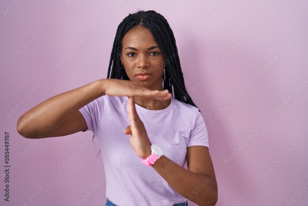 Poster African american woman with braids standing over pink background doing time out gesture with hands, frustrated and serious face