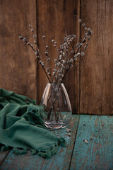 Willow branches in a glass vase. Wooden table, rustic style. Green tablecloth. Place for text.