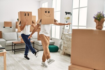 Two hispanic men couple playing with funny cardboard boxes on head at new home