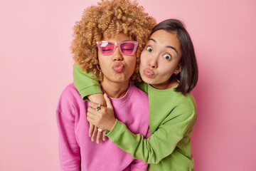 Photo of two female best friends embrace and pout lips stands closely to each other dressed in casual jumpers isolated over pink studio background have good relationships. Friendship concept