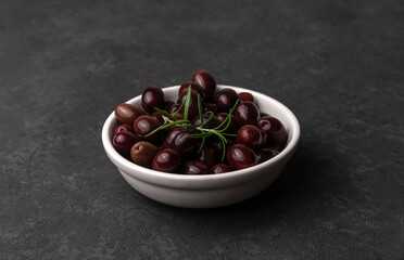 Bowl of tasty dark-purple olives on dark table with copy space