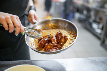 woman chef cooking chicken wings in a sauce in the kitchen © pavel siamionov