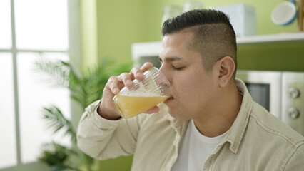 Young hispanic man drinking glass of orange juice at dinning room
