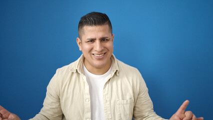 Young hispanic man smiling confident standing over isolated blue background