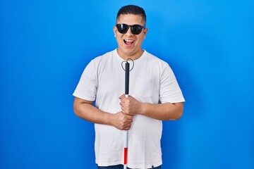 Hispanic young blind man holding cane smiling and laughing hard out loud because funny crazy joke.