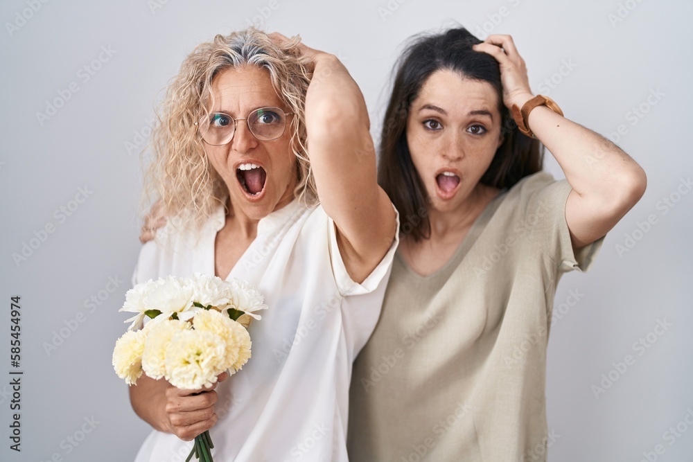 Poster Mother and daughter holding bouquet of white flowers crazy and scared with hands on head, afraid and surprised of shock with open mouth