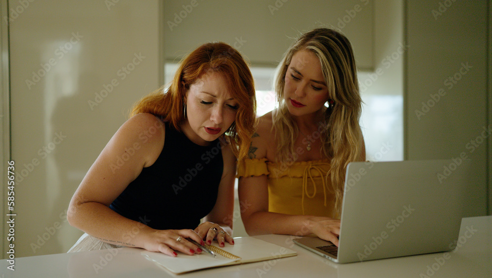 Wall mural two women using laptop writing on notebook sitting on table at kitchen