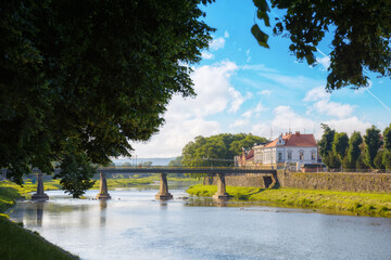 old town with river. embankment with linden trees in blossom. bridge and old buildings in the distance in morning light