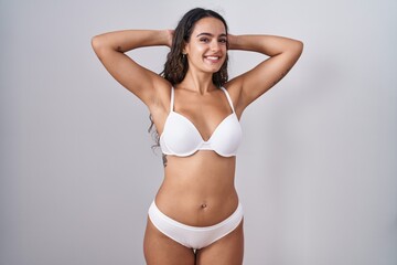 Young hispanic woman wearing white lingerie relaxing and stretching, arms and hands behind head and...