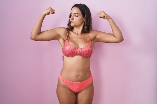 Young hispanic woman wearing lingerie over pink background showing arms muscles smiling proud. fitness concept.