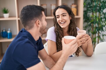 Young hispanic couple drinking coffee sitting on table at home