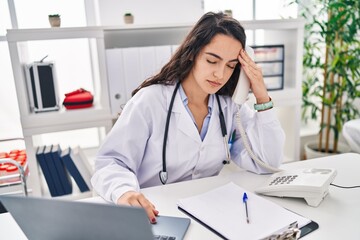 Young hispanic woman wearing doctor uniform worried working at clinic