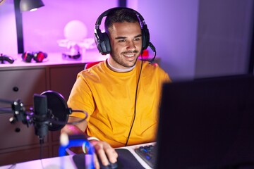 Young hispanic man streamer playing video game using computer at gaming room