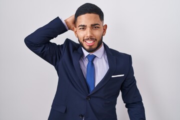 Young hispanic man wearing business suit and tie smiling confident touching hair with hand up gesture, posing attractive and fashionable