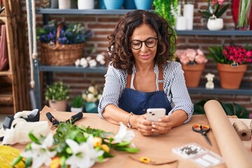 Middle age woman florist smiling confident using smartphone at flower shop