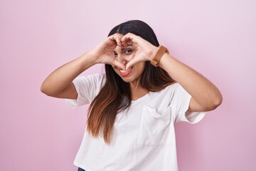Obraz na płótnie Canvas Young arab woman standing over pink background doing heart shape with hand and fingers smiling looking through sign