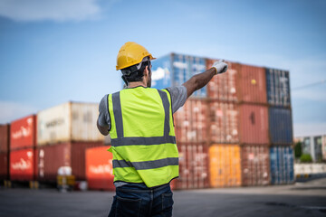 Caucasian warehouse worker in uniform with hard hat using mobile phone standing in container port...