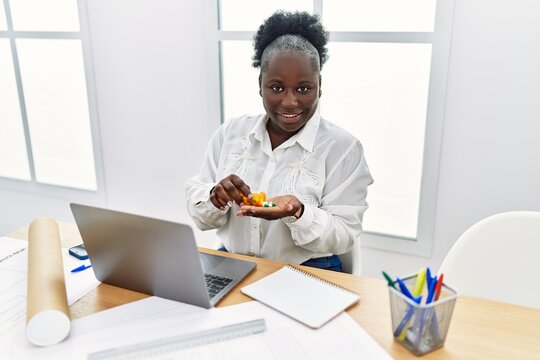 Young african american woman architect using laptop holding pills at architecture studio