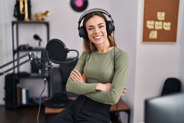 Young beautiful hispanic woman musician smiling confident sitting with arms crossed gesture at music studio