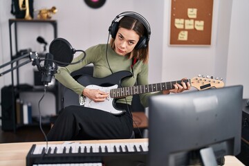 Fototapeta na wymiar Young beautiful hispanic woman musician playing electrical guitar at music studio