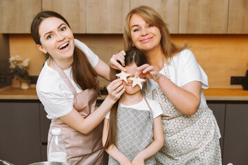 Smiling three generations of women have fun baking sweet cakes at home together. little girl with young mother and grandmother are cooking in the kitchen.