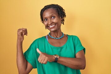 African woman with dreadlocks standing over yellow background pointing to the back behind with hand...