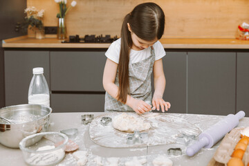 happy little girl making dough in the kitchen. a small child learns to cook food or bake yeast dough with his hands at home