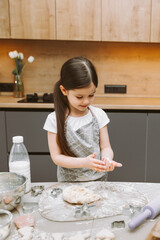 happy little girl making dough in the kitchen. a small child learns to cook food or bake yeast dough with his hands at home