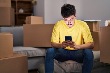 Young caucasian man using smartphone sitting on sofa at new home