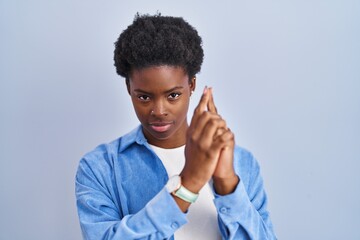 African american woman standing over blue background holding symbolic gun with hand gesture, playing killing shooting weapons, angry face