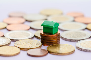 Green toy house on stable stack of coins symolizing good economy.