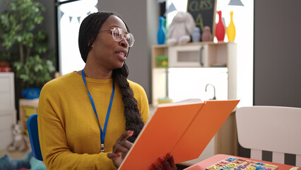 African woman preschool teacher reading a book at kindergarten