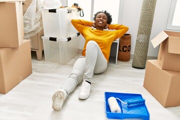 African american woman sitting on floor relaxed with hands on head at new home