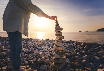 Woman building a cairn pyramide on the seashore at sunset. Zen relaxation and meditation concept