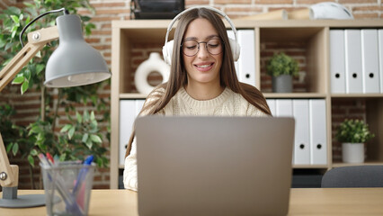 Young beautiful hispanic woman business worker using laptop and headphones working at office