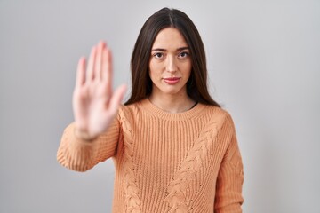 Young brunette woman standing over white background doing stop sing with palm of the hand. warning expression with negative and serious gesture on the face.