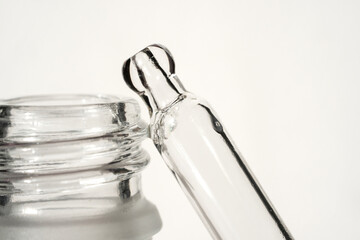Glass pipette with serum and frosted glass bottle on light background. Front view and close-up view.