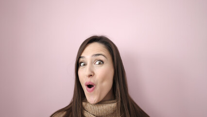 Beautiful hispanic woman standing with surprise expression over isolated pink background