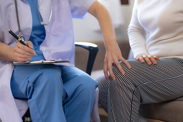 Female doctor examining the knee of an elderly Asian female patient.