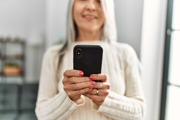 Fototapeta premium Middle age grey-haired woman smiling confident using smartphone at home
