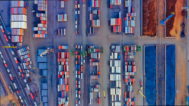 Bird's eye view of the port cargo area with containers, bulk cargo, cranes, trucks and forklifts. Evening industrial landscape at sunset.