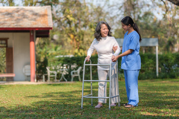 Asian nurse or a female physiotherapist is helping an elderly woman patient use a walker to learn...