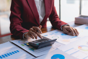 Businesswoman using calculator to check company income and budget from graph and chart.