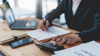 Businesswoman using calculator to check company income and budget from graph and chart.