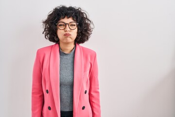 Hispanic woman with curly hair standing over isolated background puffing cheeks with funny face. mouth inflated with air, crazy expression. - obrazy, fototapety, plakaty