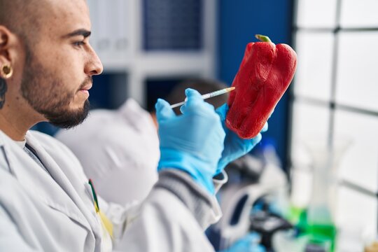 Two men scientist injecting liquid on red pepper using microscope at laboratory