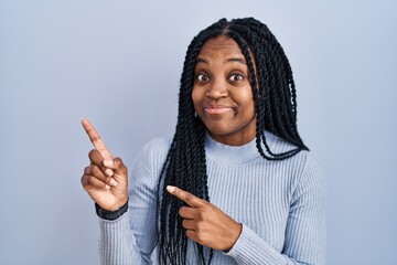 African american woman standing over blue background pointing aside worried and nervous with both...